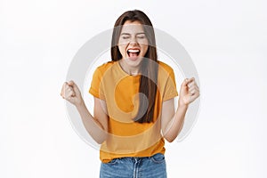 Relieved, happy woman rejoicing in yellow t-shirt, clench fists and smiling joyfully, achieve success, got lucky winning