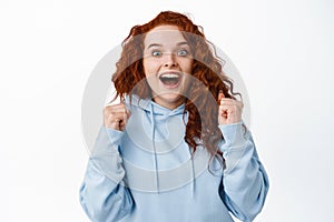 Relieved hopeful girl with red hair winning prize, gasping amazed and jumping with fist pump, celebrating victory
