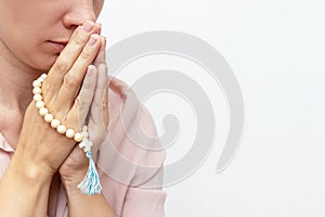 Religeous caucasian young woman praying and holding rosary in hands on white background, copy space