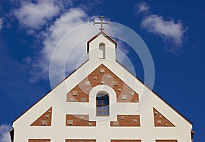 Religion symbol. Beautiful church with cross and red tile roof against a bright blue sky with flying birds and fluffy clouds.