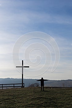 Religion theme, view of catholic cross and man silhouette, with fantastic view and mountains as background.