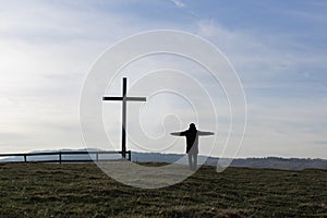 Religion theme, view of catholic cross and man silhouette, with fantastic view and mountains as background.