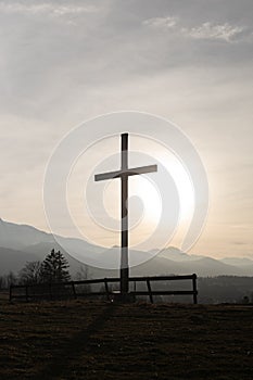 Religion theme, view of catholic cross silhouette, with fantastic sunset and mountains as background. Toned image