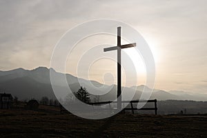 Religion theme, view of catholic cross silhouette, with fantastic sunset and mountains as background. Toned image