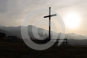 Religion theme, view of catholic cross silhouette, with fantastic sunset and mountains as background. Toned image