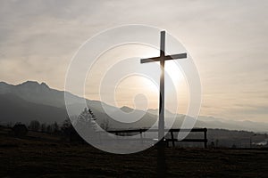 Religion theme, view of catholic cross silhouette, with fantastic sunset and mountains as background. Toned image
