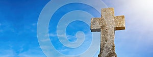 Religious Background - Blue cloudy sky withold weathered stone cross, illuminated by the sun