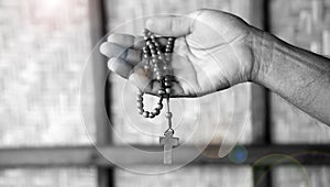 Religious background of a man holding wooden rosary in hand in black and white background.