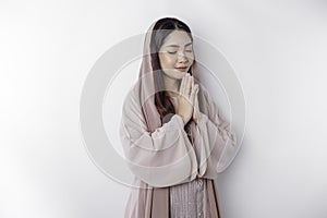 Religious beautiful Asian Muslim girl wearing a headscarf praying to God, isolated by white background