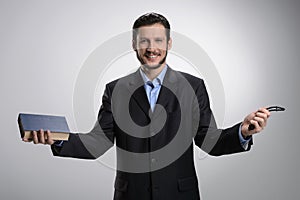 Religious businessman. Cheerful bearded man in formalwear holding the Holy Bible and rosary beads in his hands while isolated on