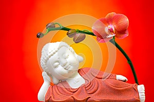 Religious concept with sleeping buddha figurine decorated with flowering red phalaenopsis orchid