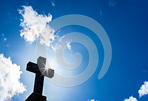 Religious cross, symbol of christianity, against blue cloudy sky with sunbeams