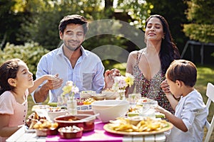 Religious Family Saying Prayers Or Grace Before Eating Outdoor Meal In Garden