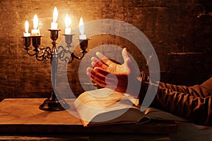 Religious female crossed hands in prayer with bible and candle