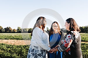 Religious grandmother, mother and daughter praying in the middle of the field on a sunny day afternoon. Family portrait.