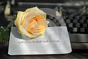 Religious inspirational quote - God removes and God replaces. Text message with yellow rose flower on white paper.