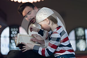 Religious Muslim Man teaching his little son to pray to God with Koran and rosary at mosque during ramadan