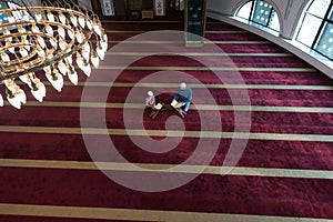Religious Muslim Man teaching his little son to pray to God with Koran and rosary at mosque during ramadan