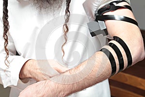 A religious orthodox with arm-tefillin on his left hand prays A jewish man is preparing the tefillin