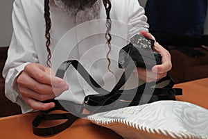 A religious orthodox with arm-tefillin on his left hand prays A jewish man is preparing the tefillin