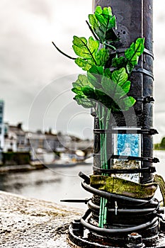 Religious prayer card tied to a metal pole with branches with green plastic leaves on a bridge