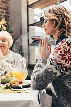 religious senior mother and daughter praying on christmas