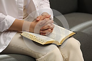 Religious woman praying over Bible indoors, closeup