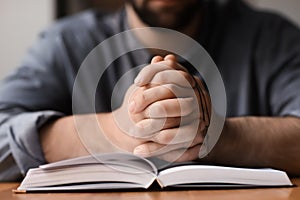 Religious young man with Bible praying at home, closeup