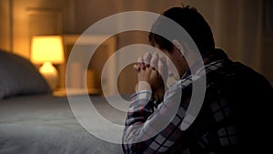 Religious young man praying in evening near bed, belief in God, Christianity