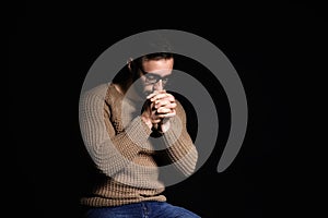 Religious young man praying to God on black background