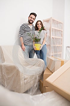 Relocating, yong couple standing in new apartment with furniture coverd with foil. photo