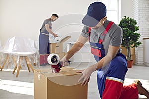 Relocation company or truck delivery worker sealing cardboard box with tape dispenser