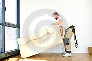 Relocation Concept. Portrait of confident male repairman moving sofa new apartment