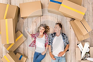 Relocation. Young couple lying on floor among boxes taking selfie on smartphone smiling happy top view