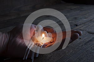 The remainder of a melted burning candle on a manÃ¢â¬â¢s hand. Love has melted. Darkness. On wooden background photo