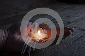 The remainder of a melted burning candle on a manâ€™s hand. Love has melted. Darkness. On wooden background