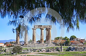 Remaining columns of the Temple of Apollo in ancient Corinth with mountains and village in background and view framed by pine tree