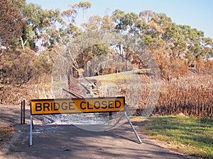 Remains of a burned down foot bridge and a warning sign after bush fire in an suburban area