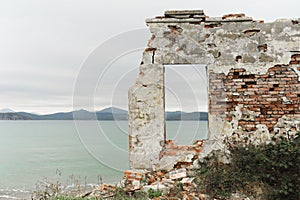 Remains of ruined old brick house and window without glass with view of beautiful blue clear sea and mountains, selective focus
