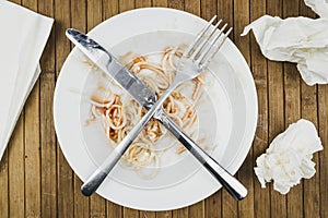 Remains of spaghetti, fork and knife on a white plate.