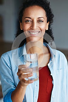 Remember to drink your eight glasses daily. Portrait of a woman drinking a glass of water at home.