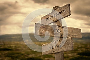 Remember to live message on wooden signpost outdoors in nature with dark moody feeling