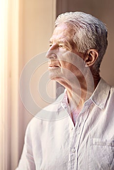 Reminded of the past, but not defined by the past. a thoughtful senior man looking out of the window at home.