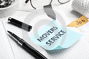 Reminder note with phrase MOVERS SERVICE and stationery on table