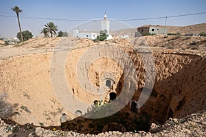 Remnants of cave dwellings in earthen pit and mosque minaret in Matmata