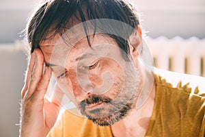 Remorse concept, regretful unkempt man at home in living room, lit by the morning sun