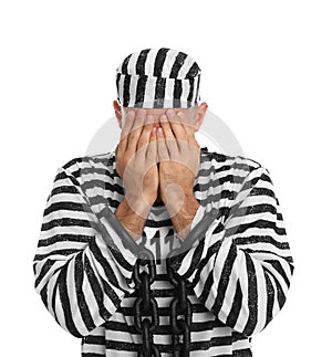 Remorseful prisoner in striped uniform with chained hands hiding his face on white background