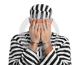 Remorseful prisoner in striped uniform with handcuffs hiding his face on white background