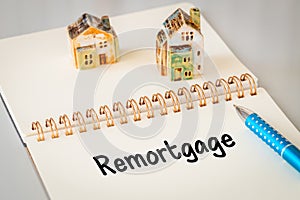 Remortgage - a word written in a notebook with a pen and a ceramic miniature of a house. Business and financial concept, copy photo