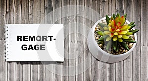 REMORTGAGE- the word is written in a notepad on a wooden background with a flower. Business and finance concept